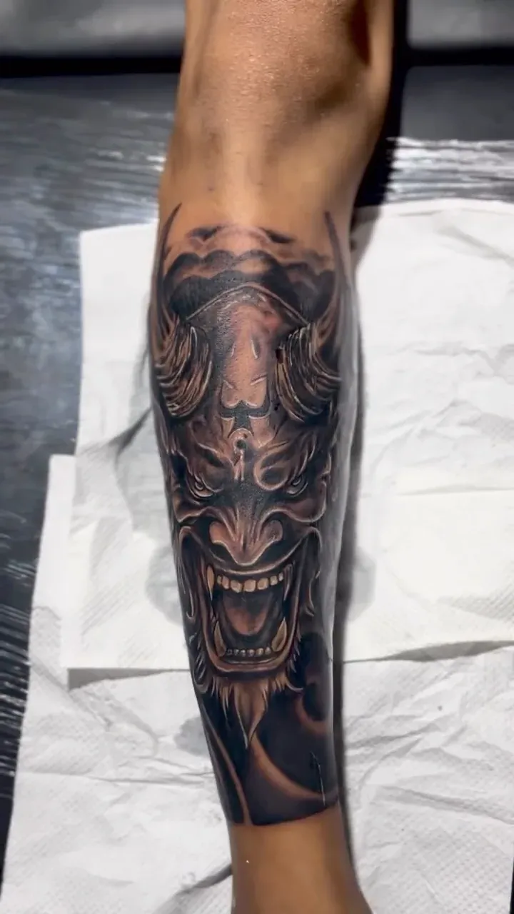 Hyper-detailed Hannya mask in blackwork realism on the side of a calf