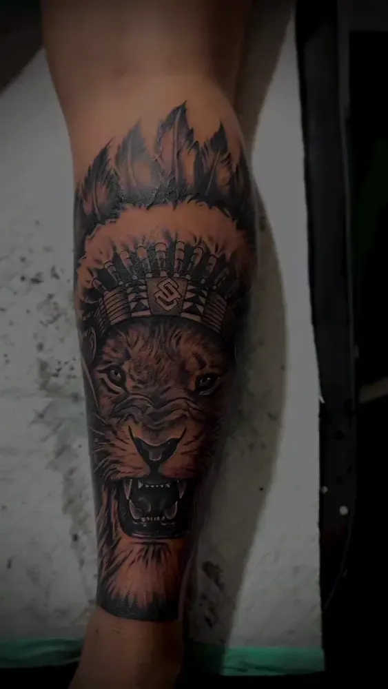 Black and grey lion head in a war bonnet, healed on a thigh